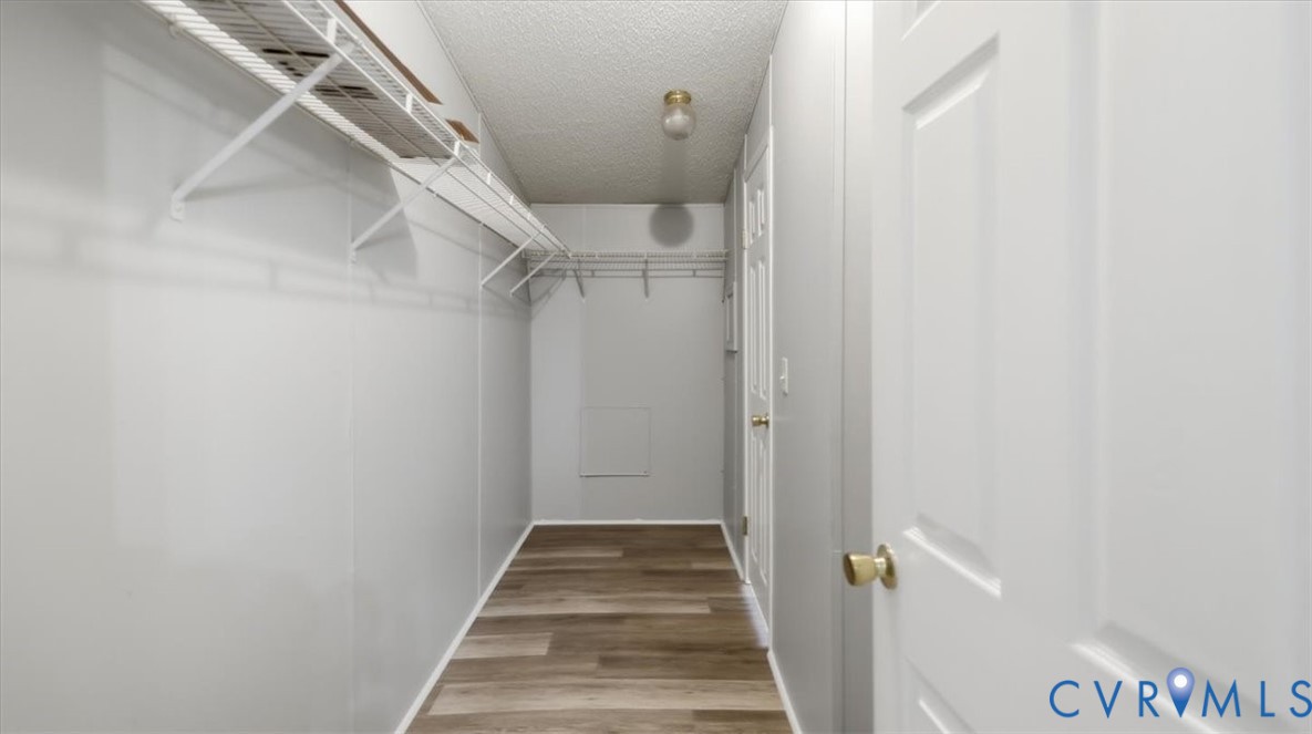 Storage area featuring wood-finish flooring, white paneled doors, tiered metal shelving, and a central ceiling-mounted light fixture