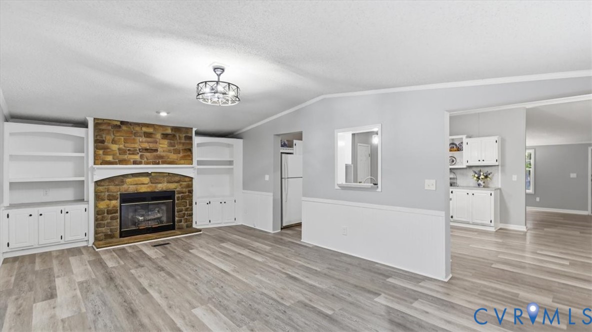 Living area featuring wood-finish flooring, a stone-accented fireplace, and built-in shelving with lower cabinetry