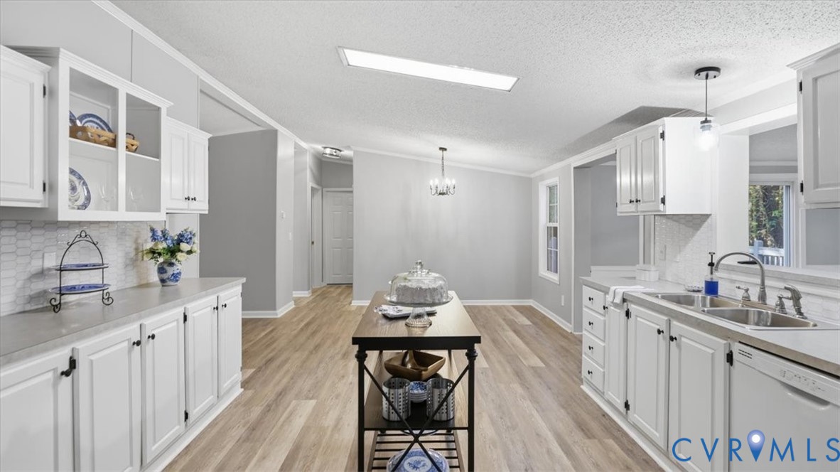 Kitchen featuring white cabinetry, glass-front upper cabinets, hexagonal tile backsplash, wood-finish flooring, and a double-basin stainless steel sink with a high-arch faucet Kitchen featuring white cabinetry, glass-front upper cabinets, hexagonal tile backsplash, wood-finish flooring, and a double-basin stainless steel sink with a high-arch faucet