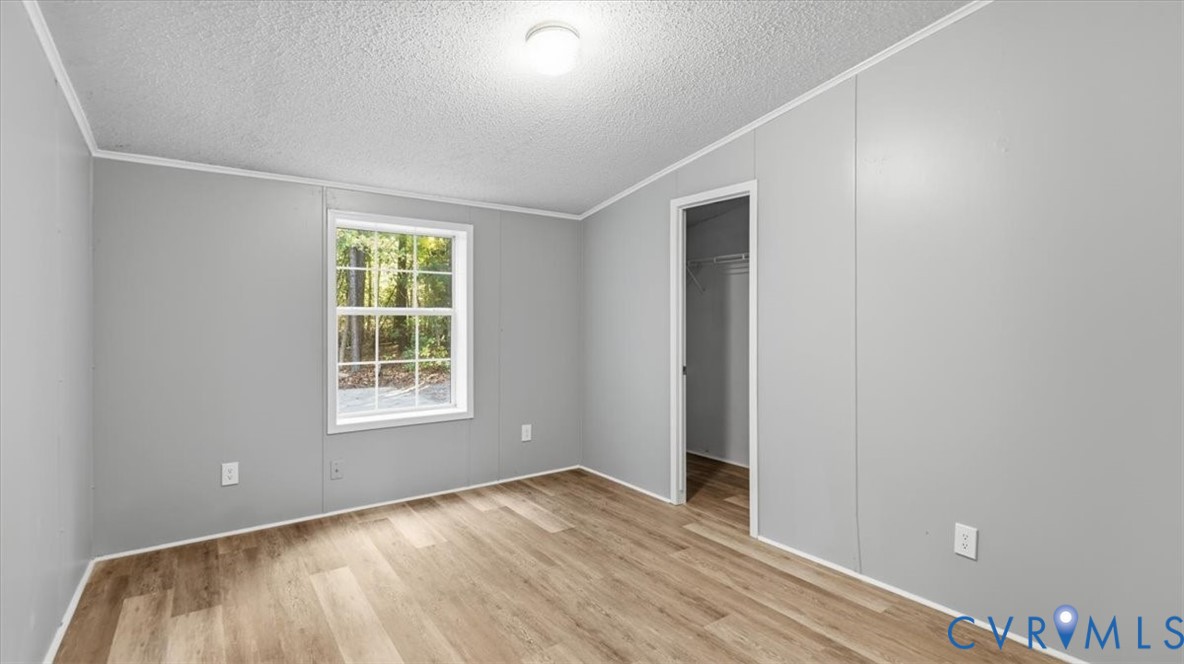 Room featuring wood-finish flooring, neutral walls, a single-hung window, and a reach-in closet with integrated shelving