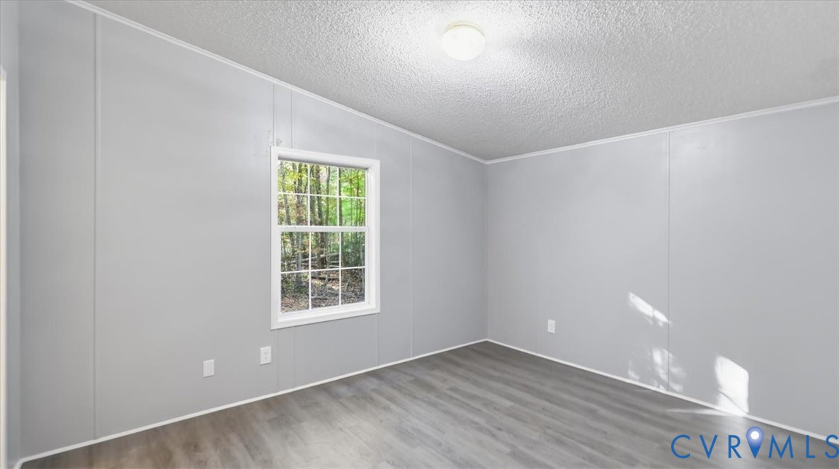 Interior room featuring neutral-toned walls, wood-finish flooring, a single-hung window with a grid pattern, and a central ceiling-mounted light fixture