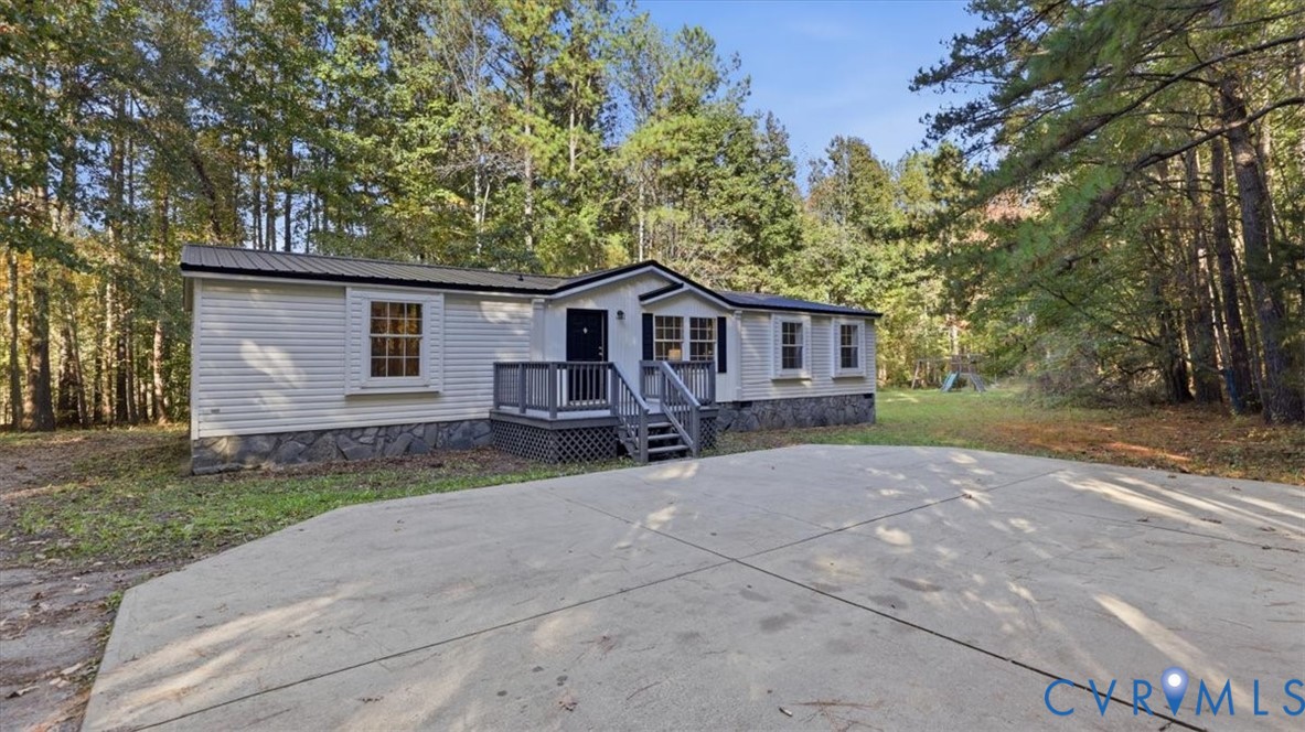 Single-level exterior featuring light-toned horizontal siding, a stone-patterned masonry foundation, a dark metal roof, and an elevated wooden entry deck