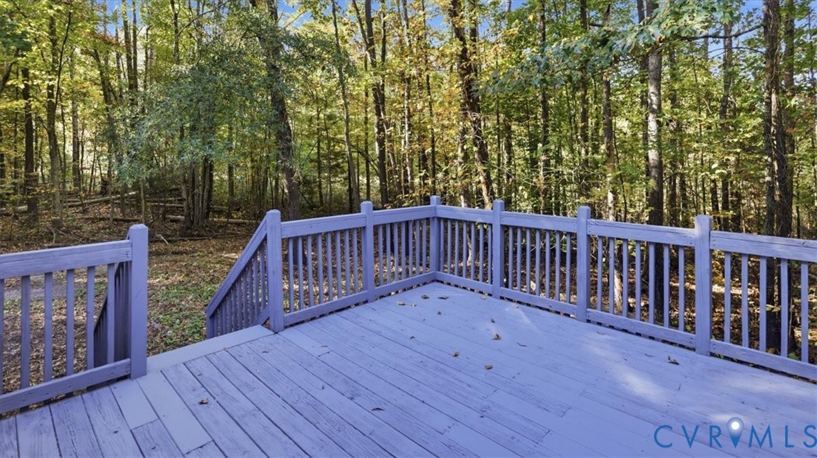 Raised wood-finish deck with vertical railing and stairs leading to a wooded lot