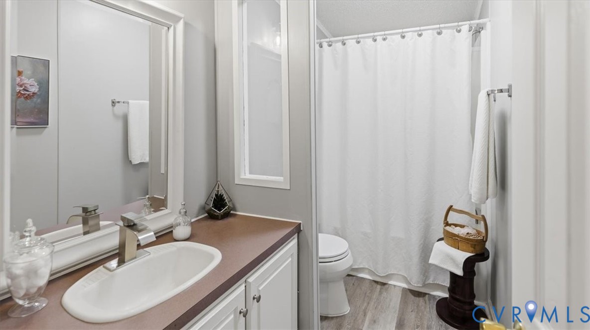 Bathroom featuring a white vanity cabinet, rectangular under-mount sink with a chrome single-handle faucet, solid-surface countertop, and wood-finish flooring