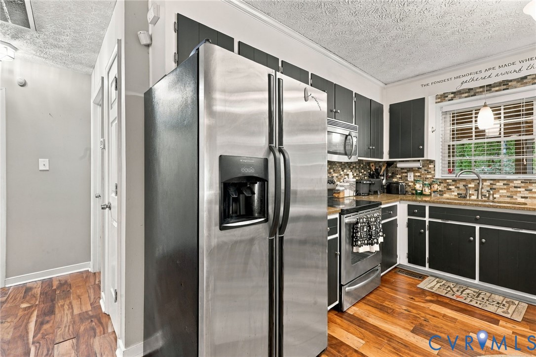 Kitchen featuring stainless steel refrigerator, microwave, and range, dark-toned cabinetry, multi-colored tile backsplash, and wood-finish flooring