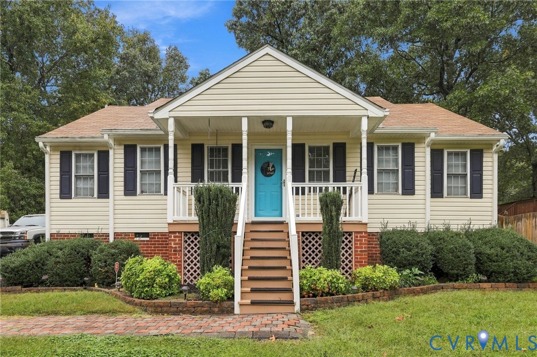 Exterior featuring light-toned horizontal siding, a covered front porch with white railing, a brick foundation, and a decorative paved walkway