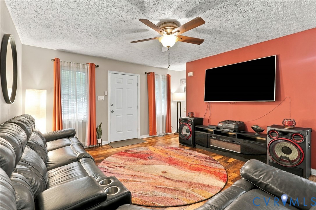 Living area featuring wood-finish flooring, a central ceiling fan with integrated lighting, and dual windows