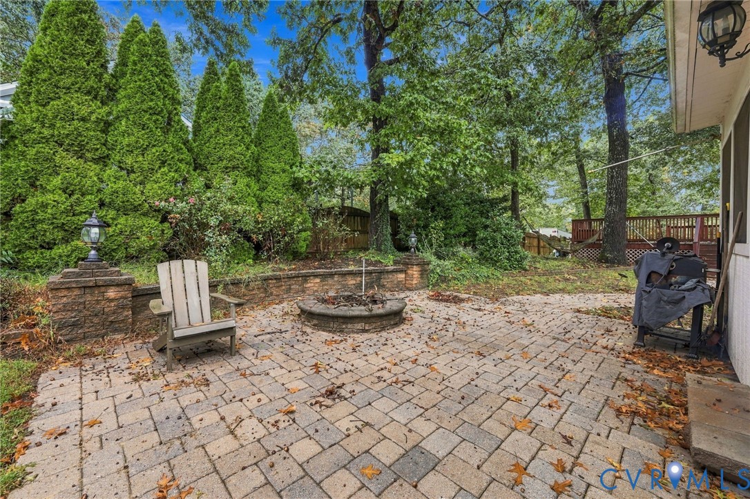 Paver patio featuring a built-in stone fire pit, retaining wall with masonry pillars, and mature perimeter landscaping