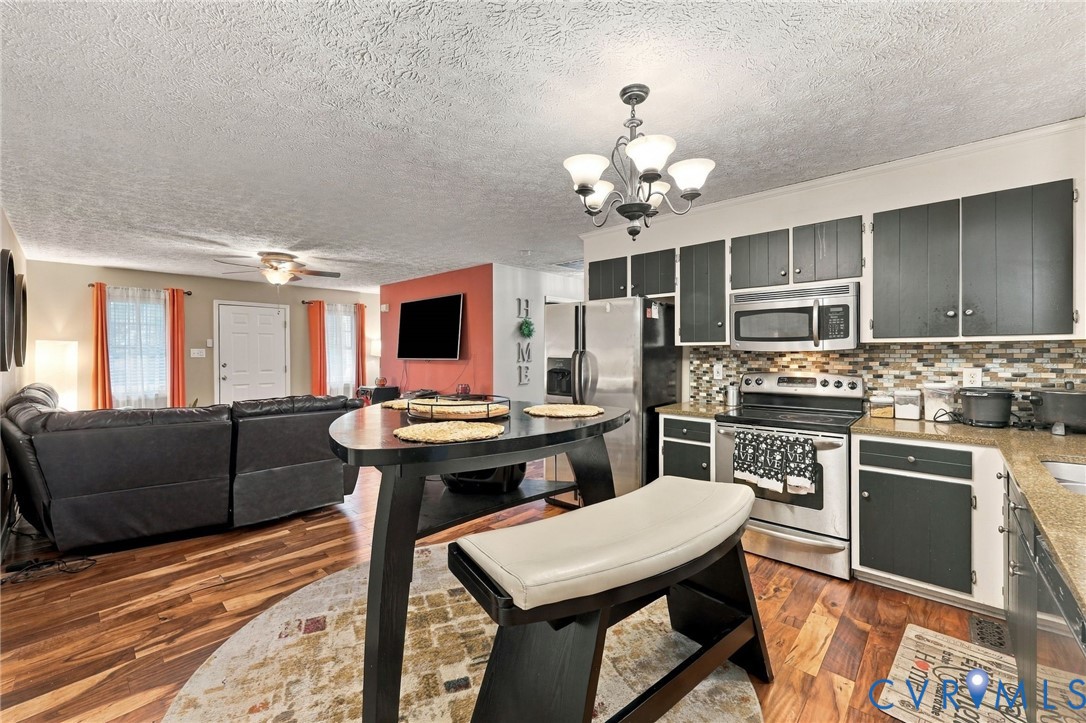 Kitchen area featuring wood-finish flooring, two-tone cabinetry, stone-tile backsplash, stainless steel appliances, and a hanging multi-light chandelier