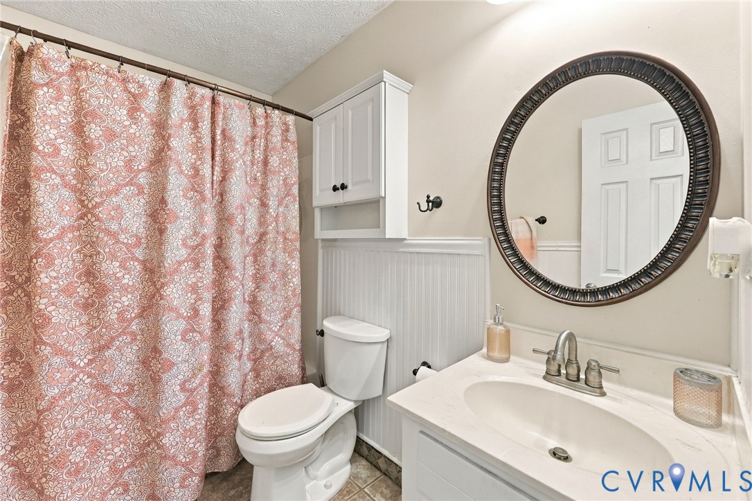 Bathroom featuring a white vanity with a neutral solid-surface countertop, an oval wall mirror with a dark metallic frame, wainscot paneling, and an upper built-in storage cabinet