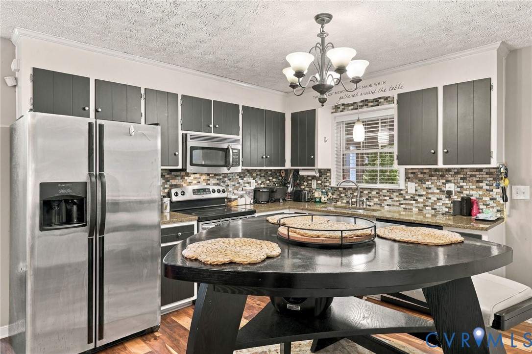 Kitchen featuring two-tone cabinetry, stainless steel appliances, multi-colored tile backsplash, stone-finish countertops, and an integrated multi-tiered island