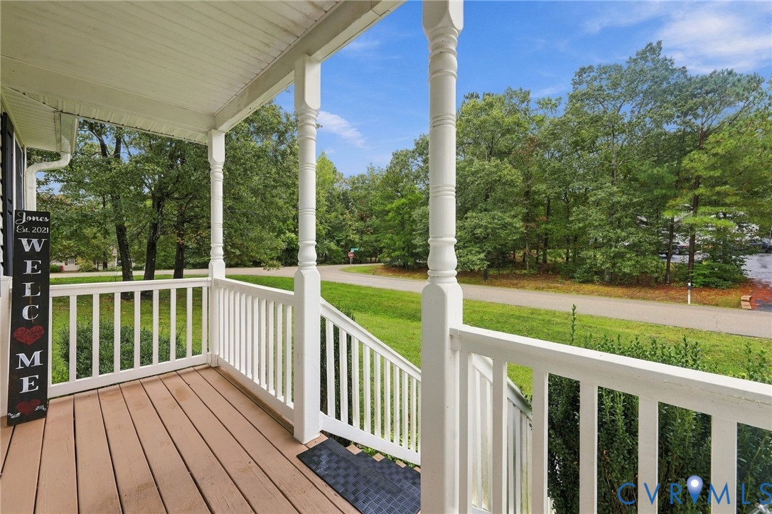 Covered front porch featuring wood-finish flooring, decorative white columns, and a white wood railing