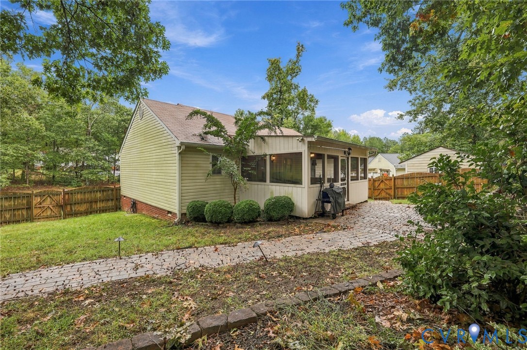 Exterior featuring a screened-in porch, light-toned horizontal siding, paver stone walkway, and wood-paneled privacy fencing