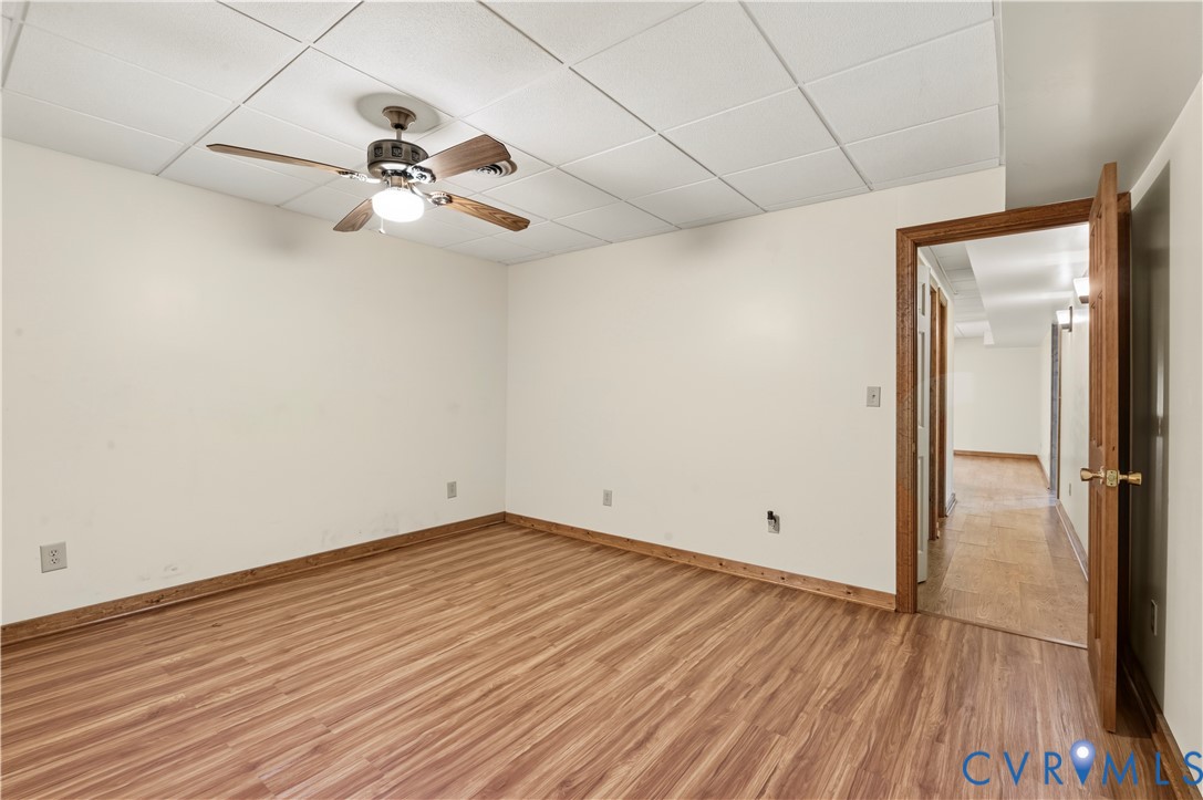 Interior space featuring wood-finish flooring, a suspended acoustic tile ceiling, and a central ceiling fan with integrated lighting