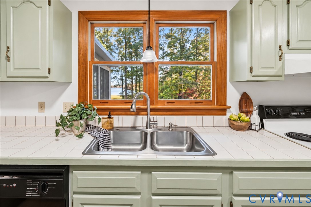 Kitchen featuring painted cabinetry, tiled countertops, a double-basin stainless steel sink with a high-arch pull-down faucet, and a wood-framed window with exterior scenery