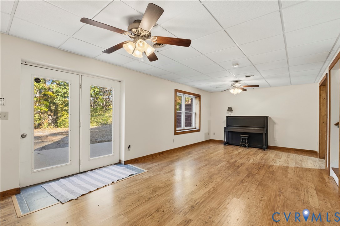Spacious room featuring wood-finish flooring, drop ceiling with dual ceiling fans, white glass-paneled double doors, and natural lighting provided by a window