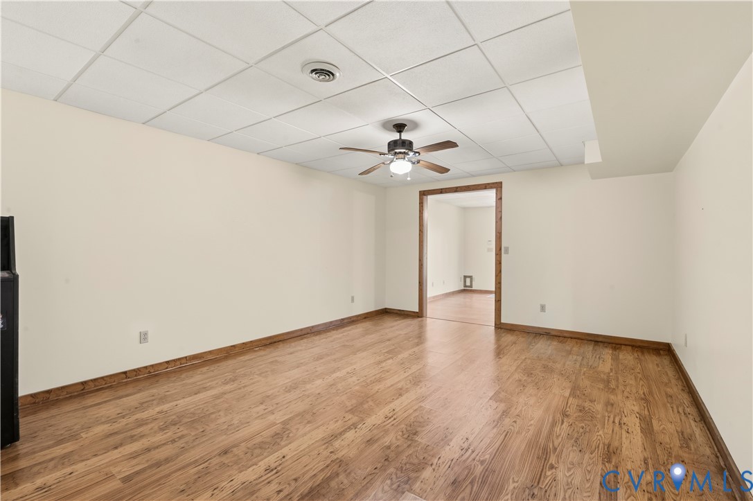 Interior space featuring wood-finish flooring, a suspended acoustic tile ceiling, and a central ceiling fan with an integrated light fixture