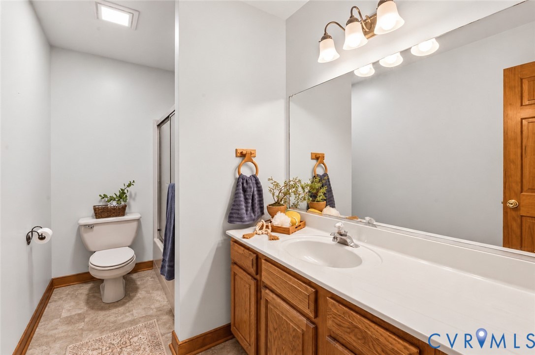 Bathroom featuring a wood-finish vanity with a molded white countertop and integrated sink, full-width wall mirror, tri-light fixture, and shower enclosure