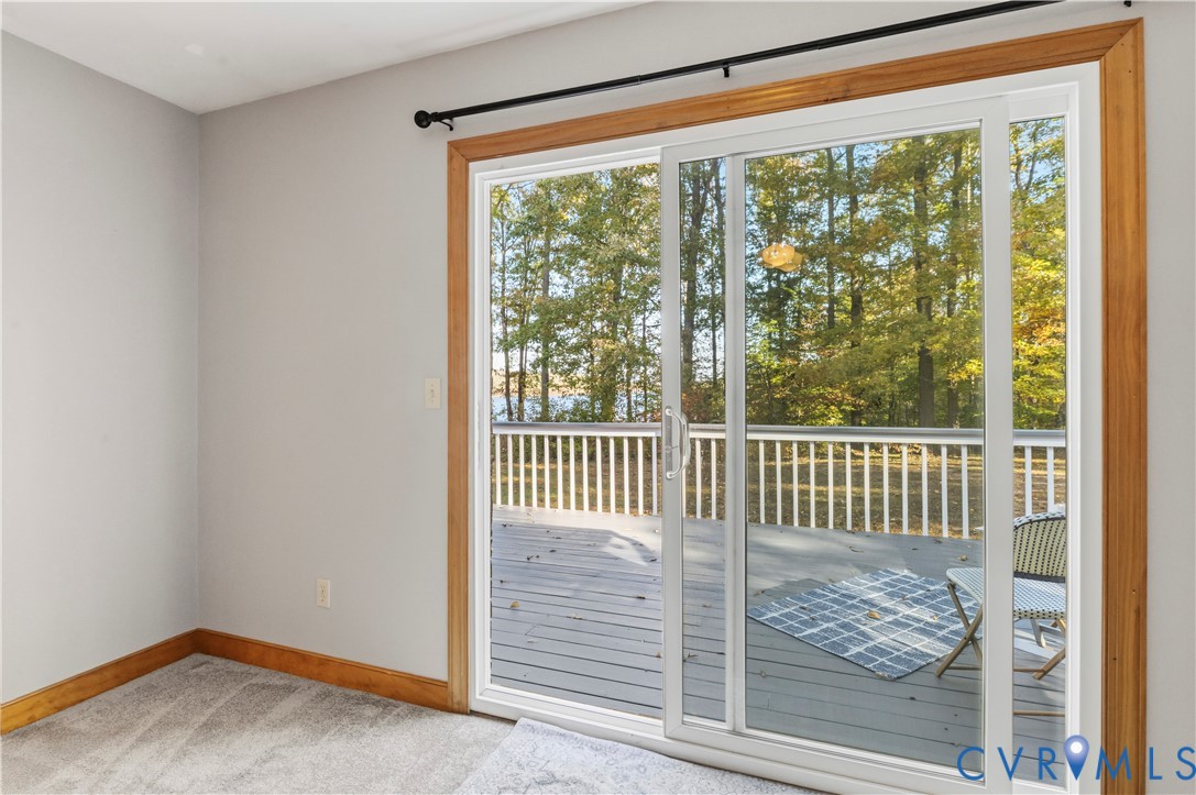 Sliding glass door with natural wood casing, revealing an exterior deck with white railing and surrounding tree foliage