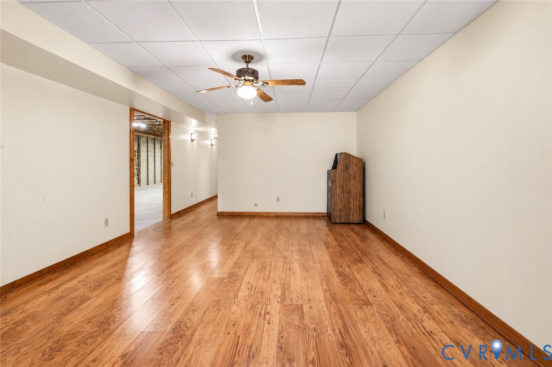 Finished interior room featuring wood-finish flooring, a dropped ceiling, and a central ceiling fan with integrated lighting