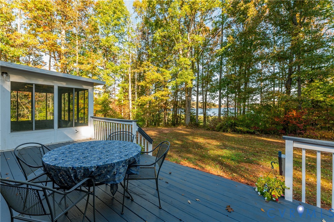 Painted wood deck featuring a white railing and an enclosed sunroom with large windows, overlooking a wooded yard and water