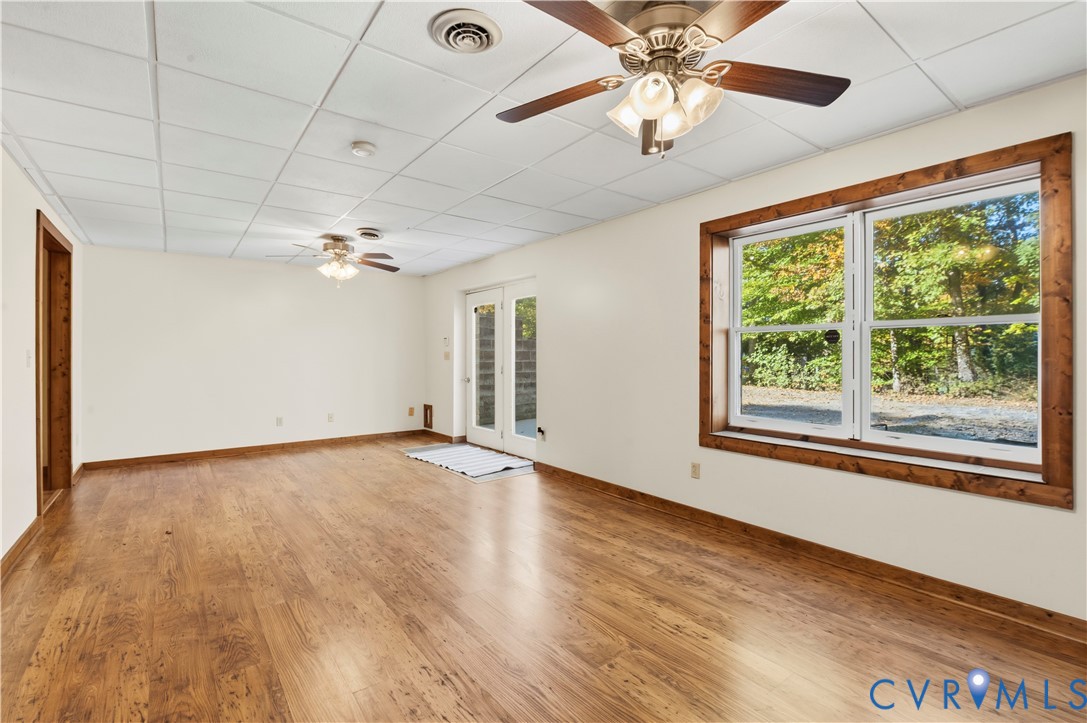 Interior space featuring wood-finish flooring, dual ceiling fans, a drop ceiling, and a large window framed in natural wood trim