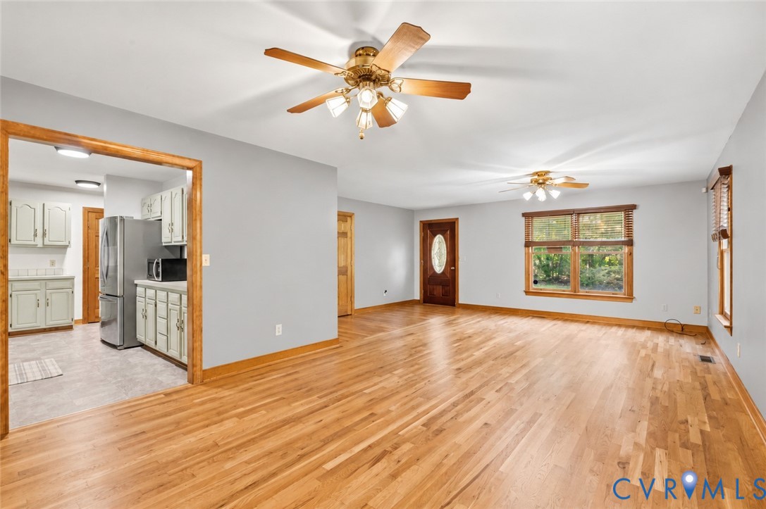 Open living area featuring wood-finish flooring, natural wood trim, dual ceiling fans, and a solid wood entry door with an oval glass insert