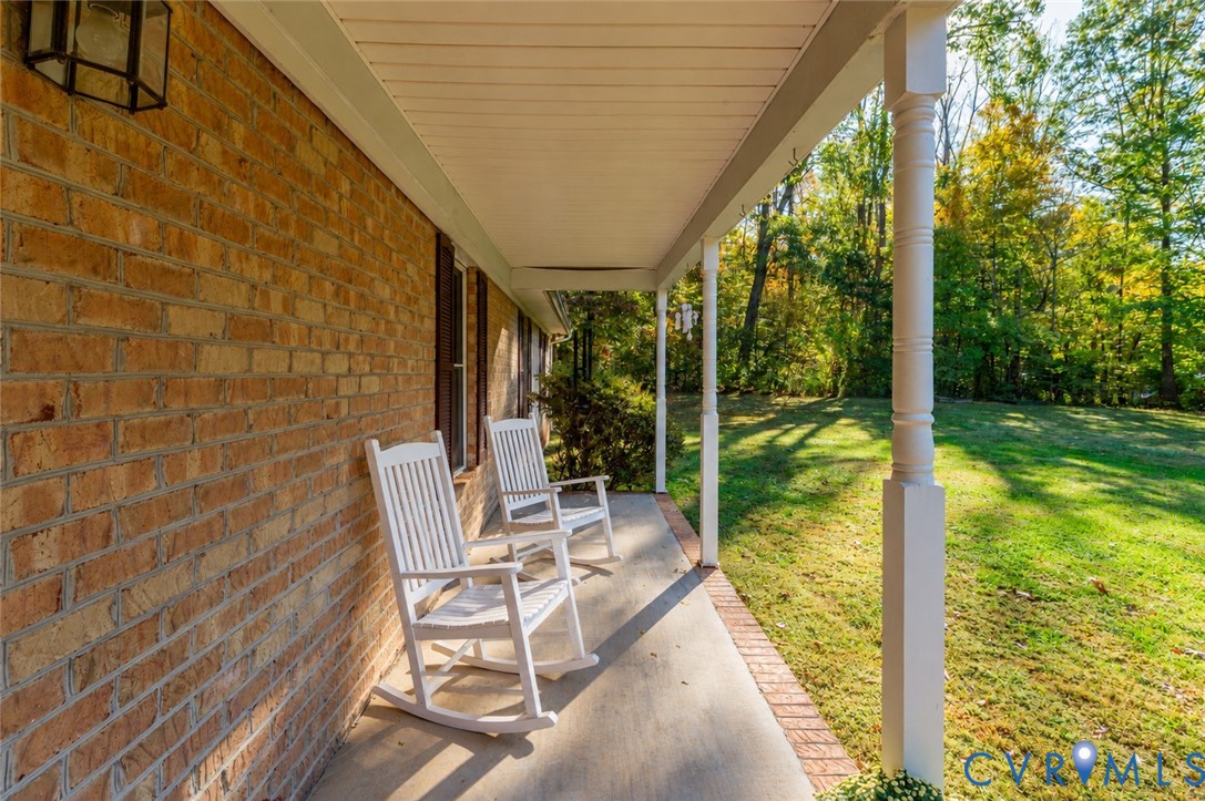 Covered porch featuring a brick exterior facade, concrete flooring, decorative wood columns, and an attached wall-mounted lantern