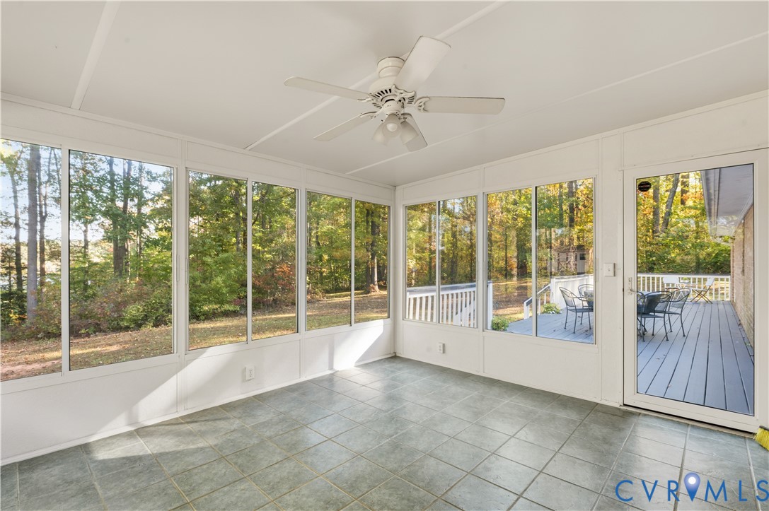 Enclosed sunroom featuring large paneled windows, tiled flooring, a ceiling-mounted fan, and a glass-paneled exterior door