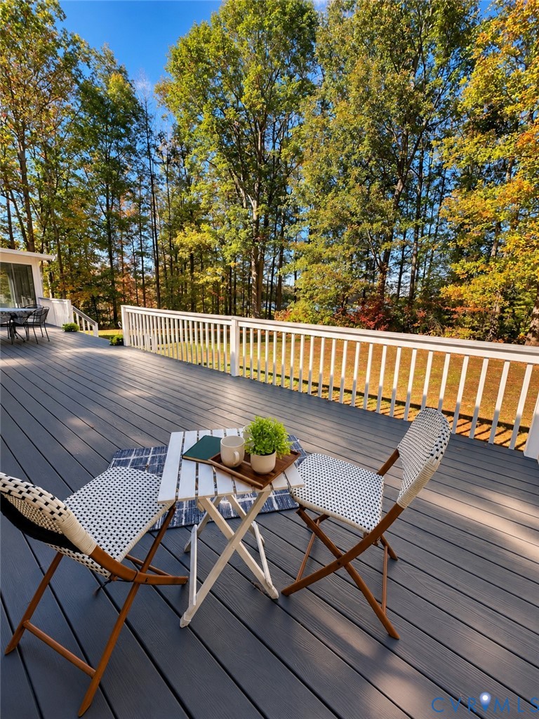 Expansive wood-finish deck with white vertical-spindle railing, set against a backdrop of mature trees