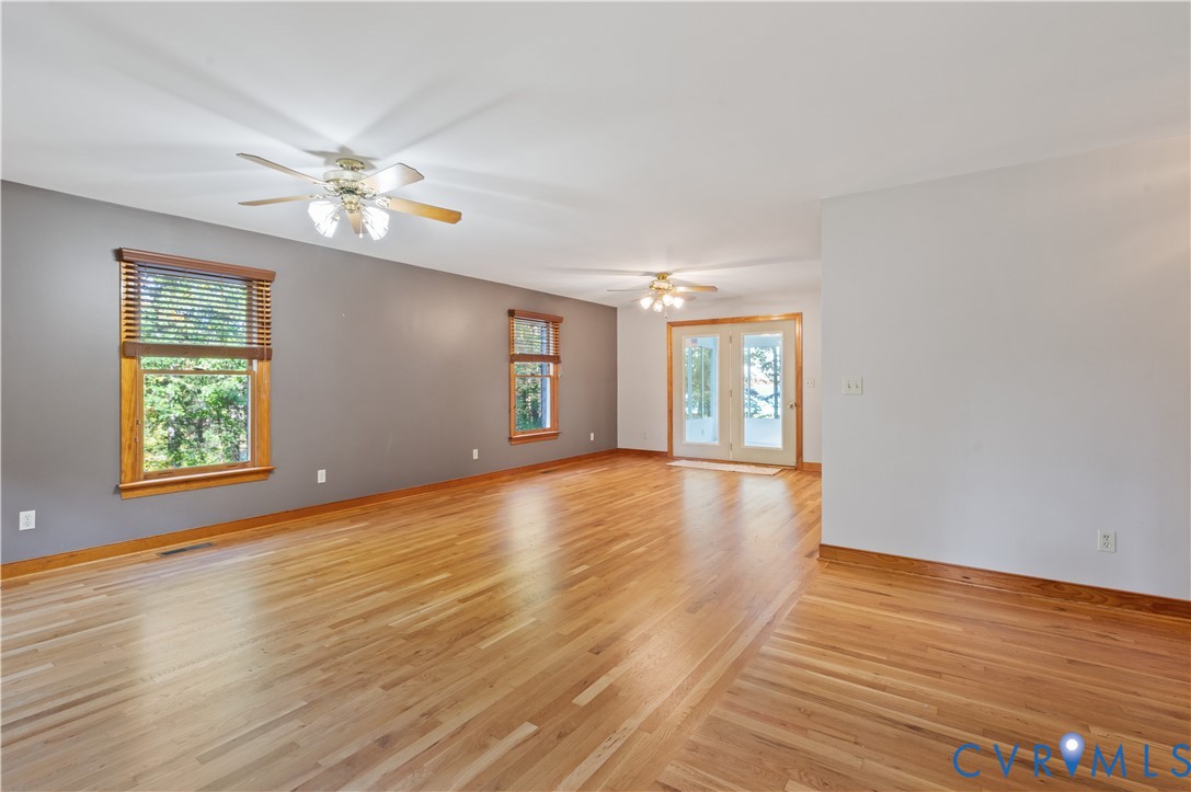 Spacious interior featuring wood-finish flooring, dual ceiling fans with integrated lighting, wood-framed windows, and glass-paneled exterior doors