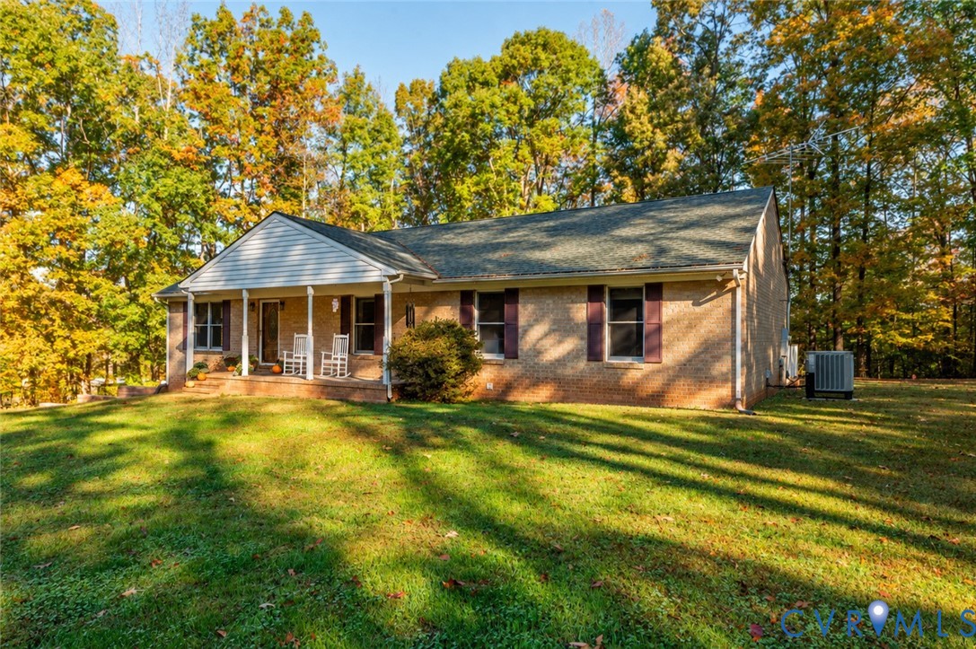 Brick exterior featuring a covered front porch, dark-toned shutters, and mature wooded surroundings