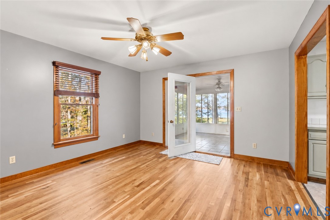 Room featuring wood-finish flooring, natural wood trim, a ceiling fan with integrated lighting, and a glass-paneled door