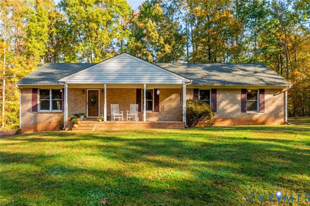 Single-story brick exterior featuring a covered front porch, gabled roofline, and mature wooded surroundings