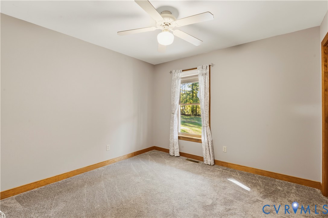 Neutral-toned interior space featuring carpeting, a white ceiling fan with integrated lighting, and a single-pane window with wood trim