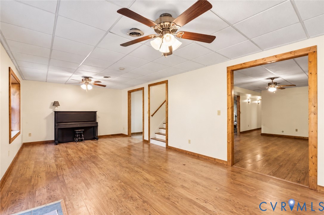 Interior space featuring wood-finish flooring, drop ceiling panels, multi-light ceiling fans, and natural wood-trim doorways