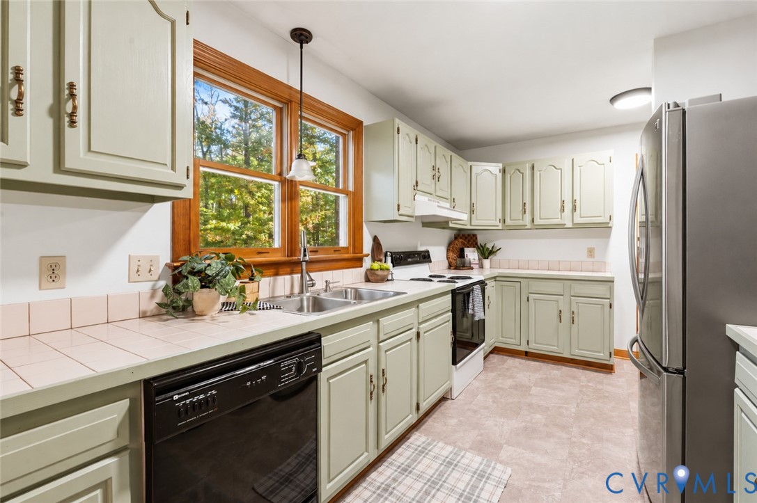 Kitchen featuring custom cabinetry, tile countertops, a double basin stainless steel sink, wood-trimmed window, and pendant lighting