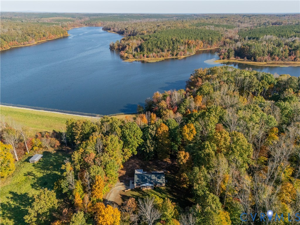Aerial perspective of expansive wooded acreage featuring direct waterfront access, a primary structure with a metal roof, and a private gravel drive