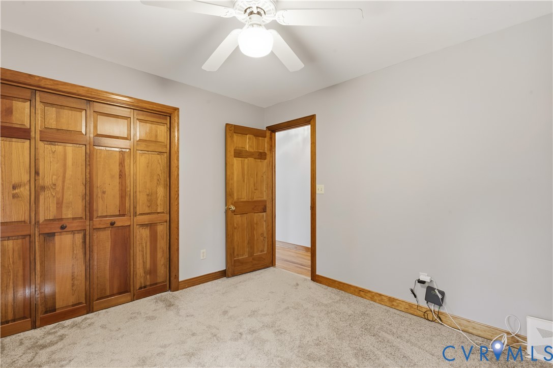 Neutral-toned carpeted flooring, wood-finish closet doors, six-panel wood door, and a ceiling-mounted light fixture with a multi-blade fan