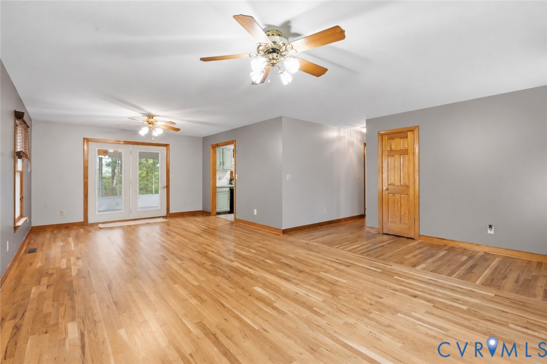 Open-concept interior featuring wood-finish flooring, neutral wall paint, dual ceiling fans, and glass-paneled double doors