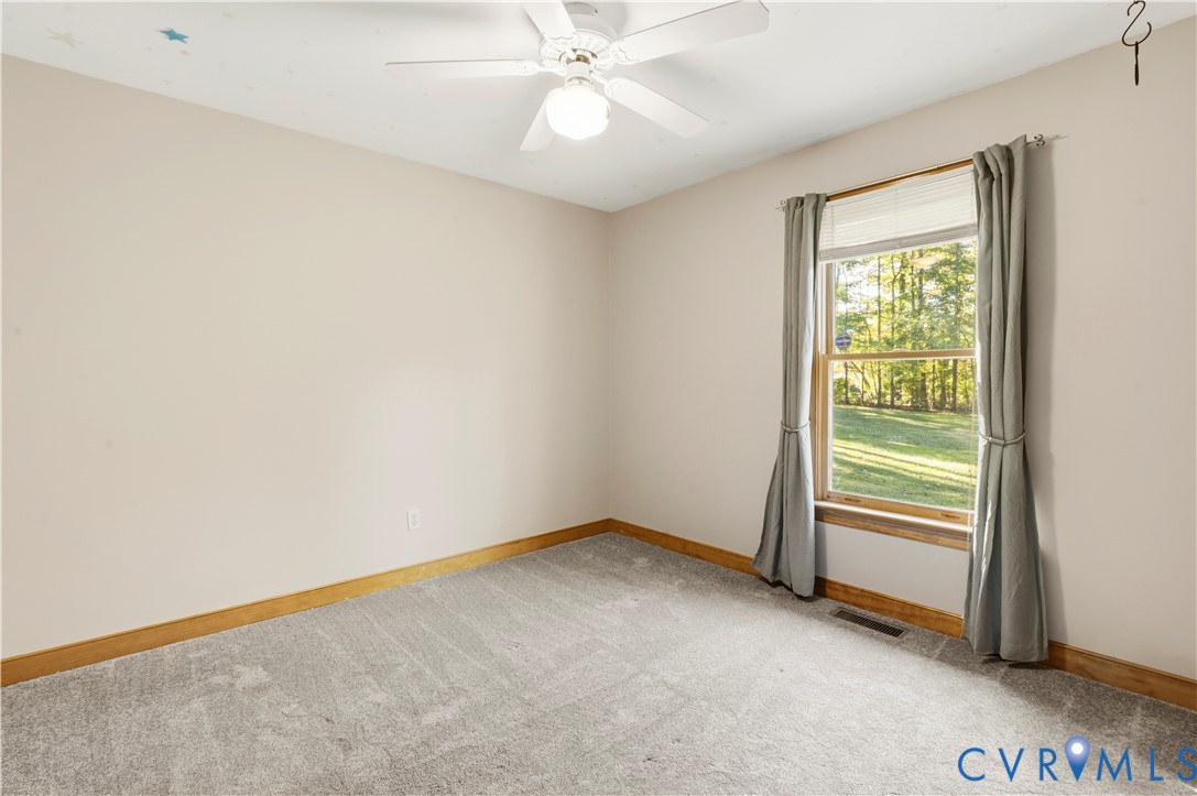 Neutral-toned carpeting, wood trim, white ceiling fan with integrated light fixture, and a single-pane window