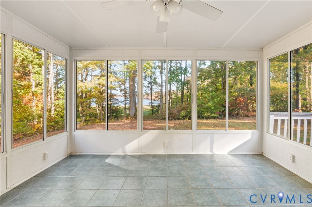 Enclosed sunroom featuring expansive windows, tile flooring, and a ceiling fan with integrated lighting
