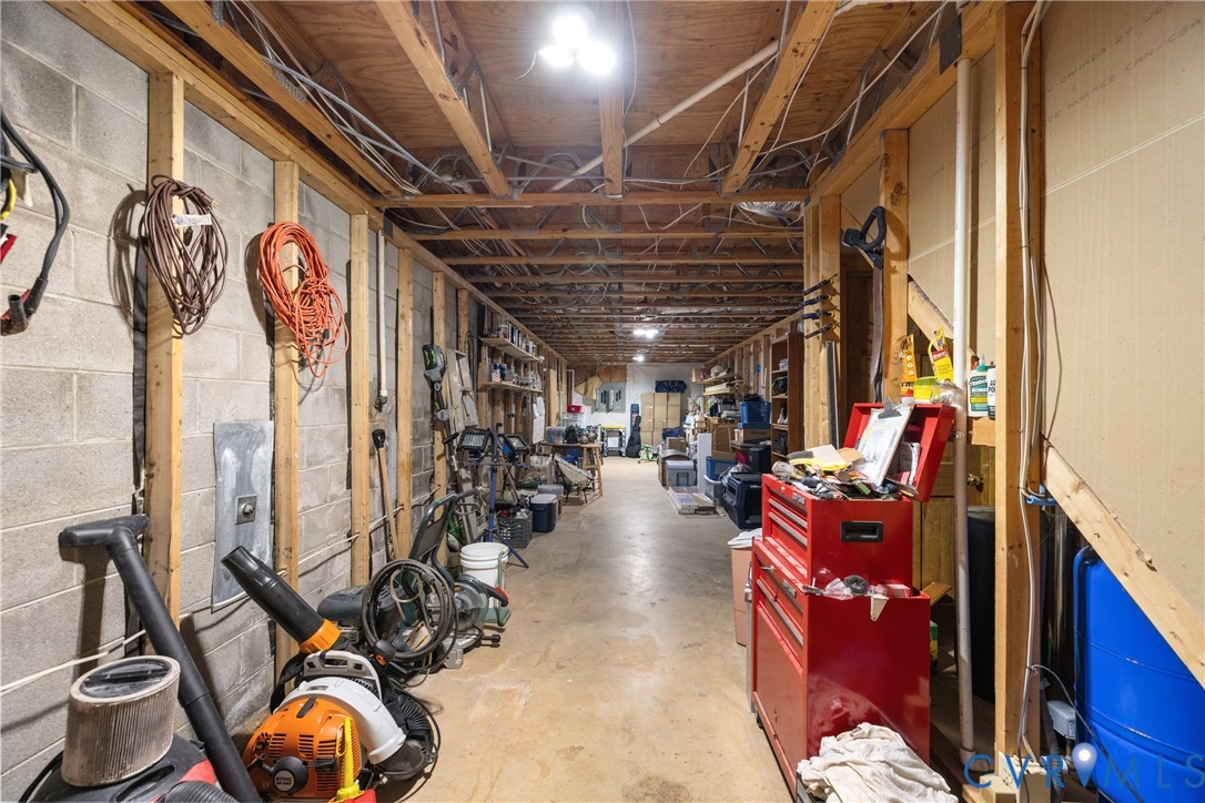 Unfinished storage space featuring exposed timber joists, concrete masonry unit walls, and concrete flooring