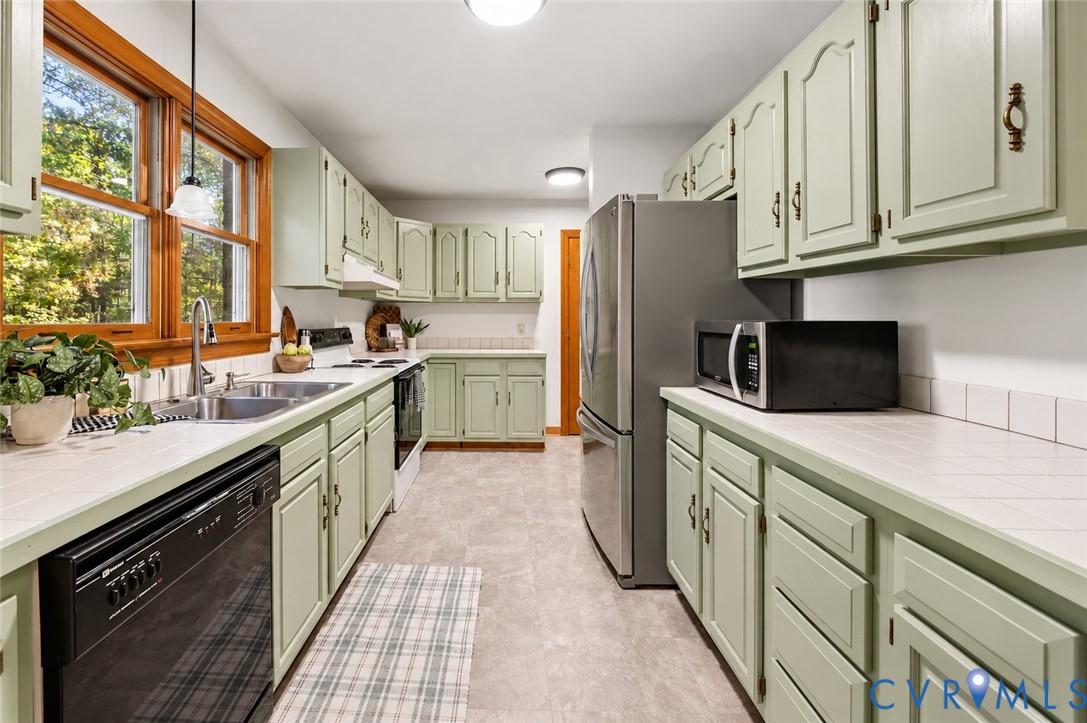 Kitchen featuring painted cabinetry, tiled countertops, double-basin stainless steel sink with pull-down faucet, and wood-framed window