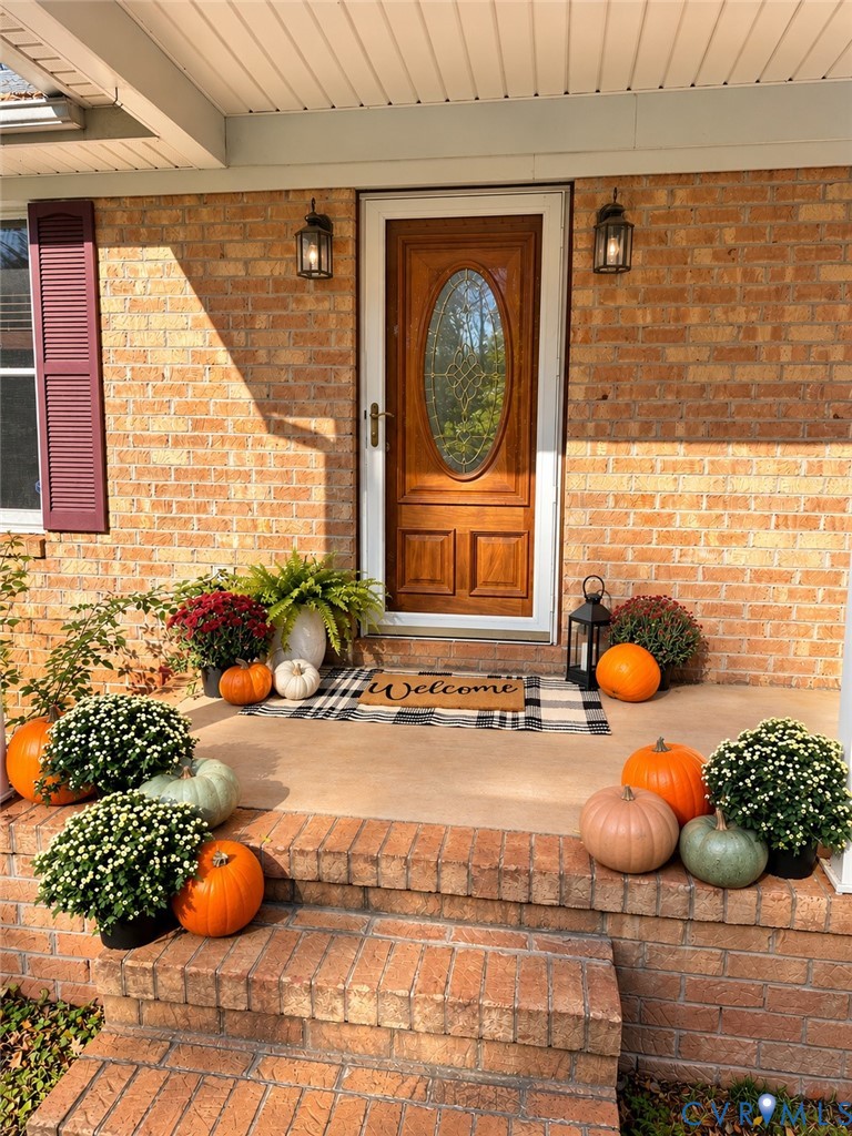Front entrance featuring a brick facade, solid wood entry door with an oval glass inset, tiered brick steps, and wall-mounted exterior lanterns