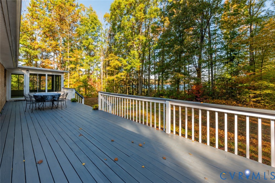 Expansive deck with white railings, screened-in porch, and mature trees