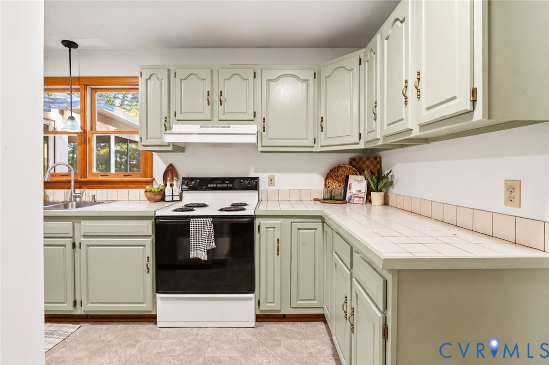 Kitchen featuring sage green cabinetry, white tiled countertops, tiled backsplash, built-in range, and a dual-basin stainless steel sink with a goose-neck faucet
