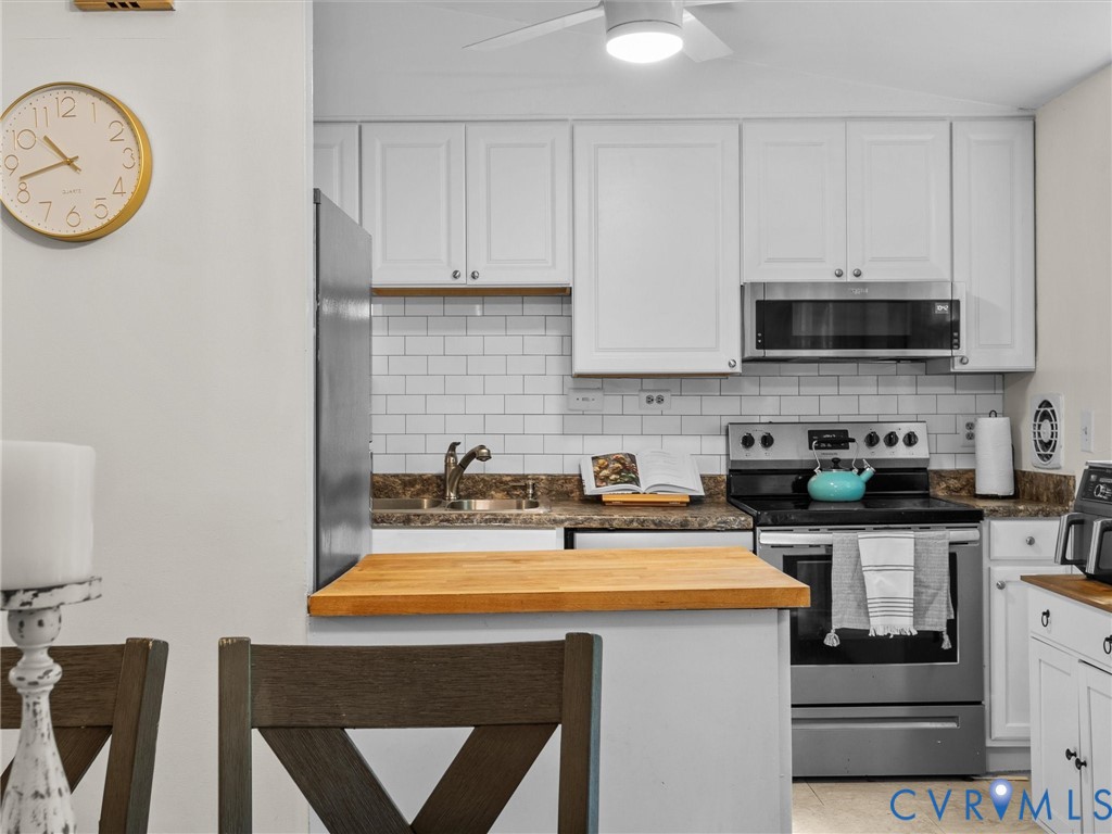 Kitchen featuring white cabinetry, a white subway tile backsplash, butcher block countertop, stainless steel appliances, and an undermount sink