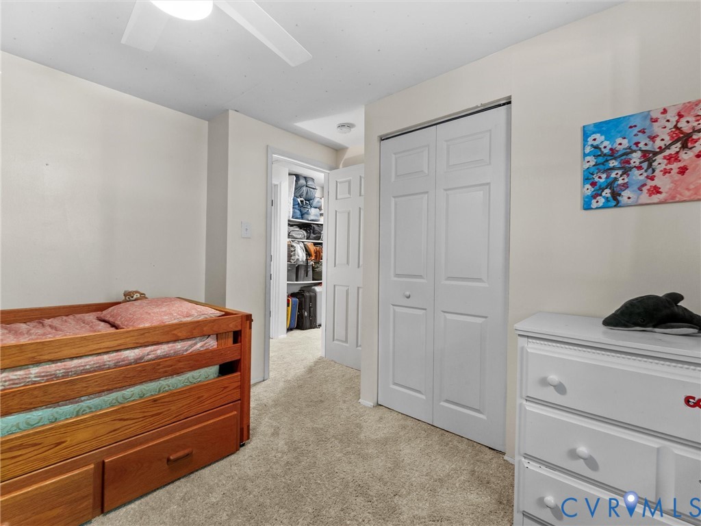 Neutral-toned room featuring wall-to-wall carpeting, a white paneled closet door, a ceiling fan, and a walk-in storage area with integrated shelving