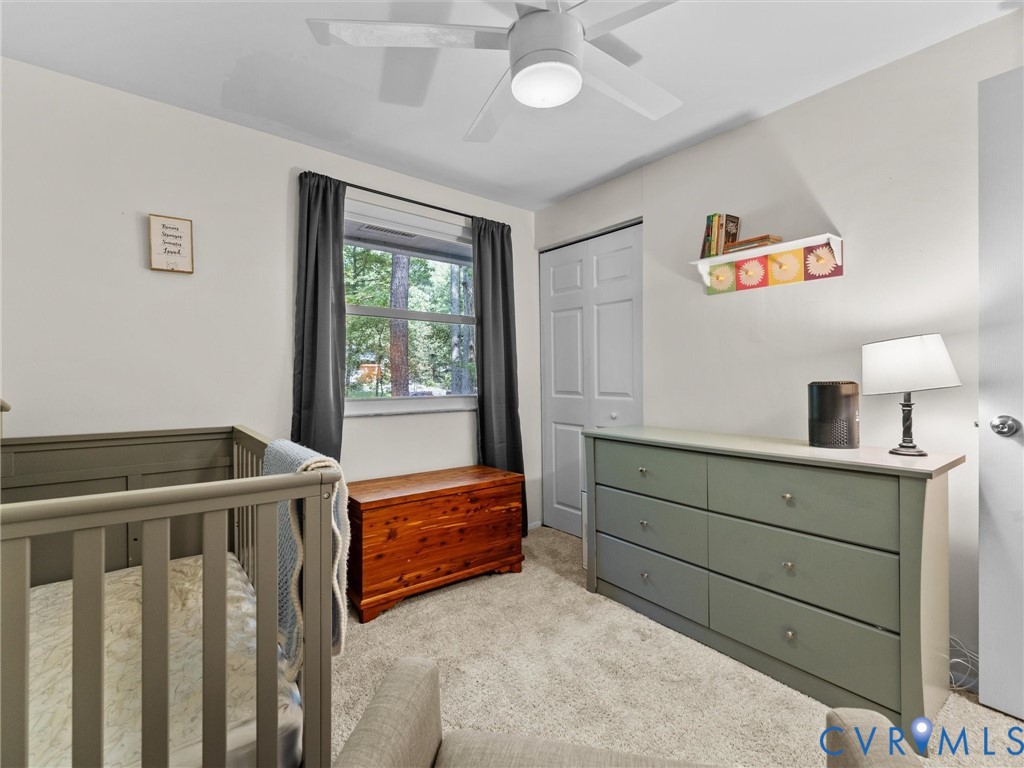 Neutral-toned interior featuring carpeted flooring, a ceiling fan with integrated lighting, a single-pane window, and a built-in closet with paneled doors